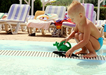 a little boy of European appearance plays in the summer near the pool with water in the water park.