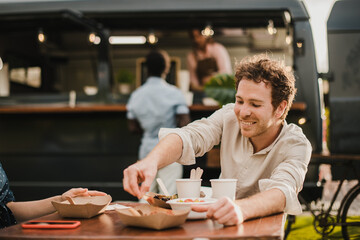 Young happy people eating at food truck outdoor - Focus on man face