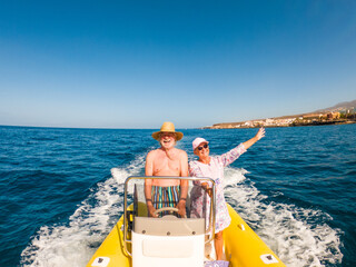 Beautiful and cute couple of seniors or old people in the middle of the sea driving and discovering new places with small boat. Mature woman holding a phone and taking a selfie with hew husband.