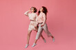 Two laughing girls holding hands. Studio shot of female friends running on pink background.