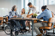 © Dragana Gordic - Happy businessman in wheelchair reading documents during a meeting with his colleagues in the office. Shot of a team of businesspeople having a meeting in a modern office