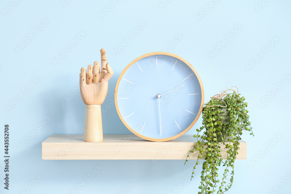 Shelf with wooden hand and clock hanging on color wall