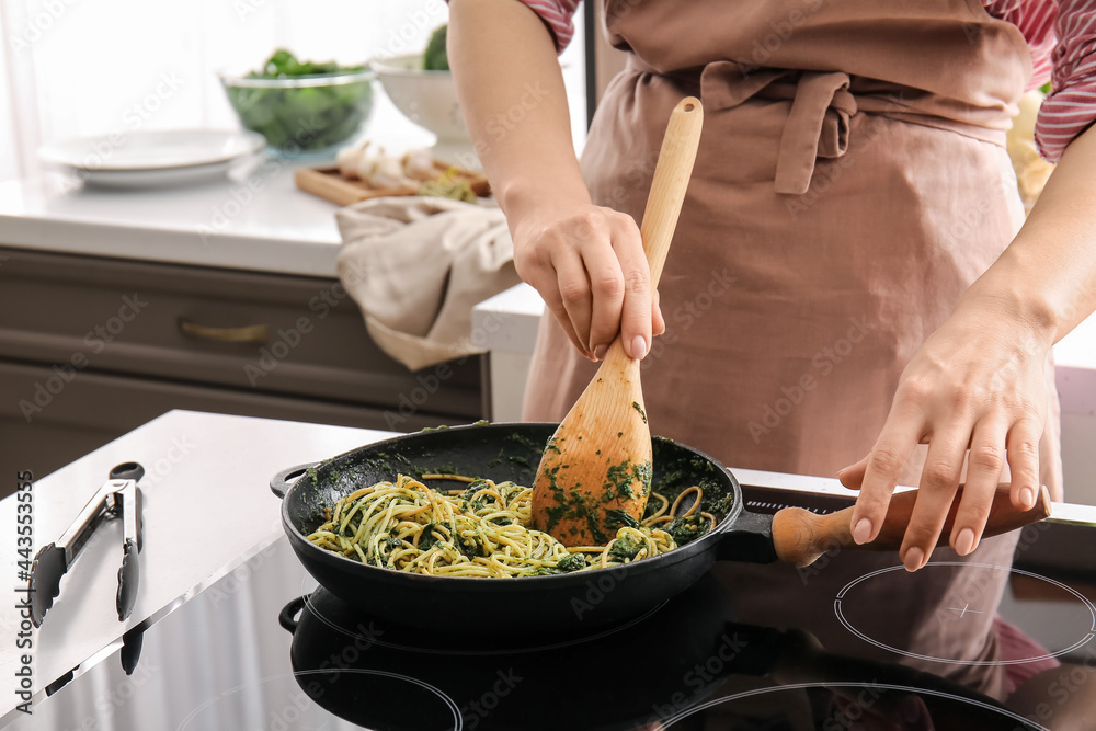 Woman cooking tasty pasta with spinach in kitchen