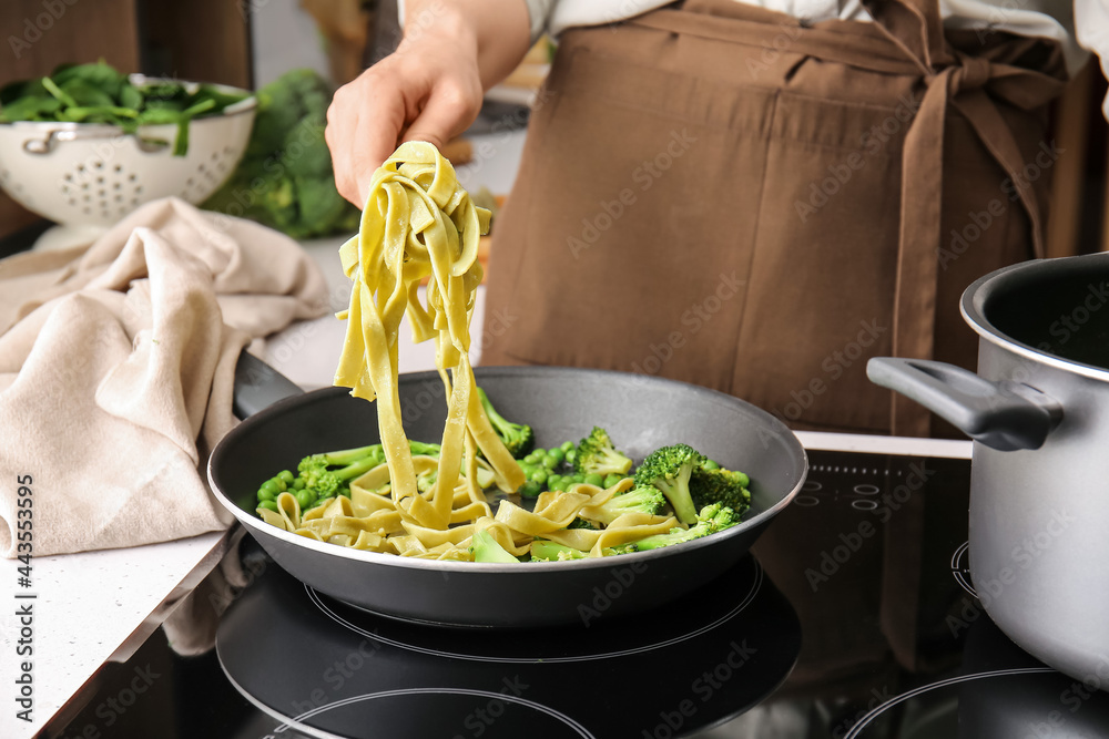 Woman cooking tasty pasta with vegetables in kitchen