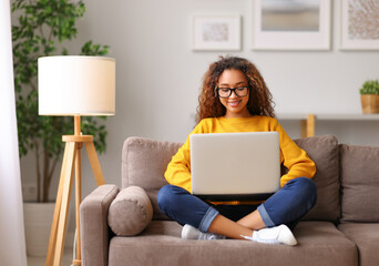 Smiling african american young woman using laptop while working remotely or studying online from home