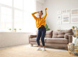 Young playful african american woman in headphones jumping and dancing in living room at home