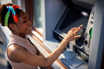 Beautiful african women using ATM machine. Attractive young woman withdrawing money from credit card at ATM.