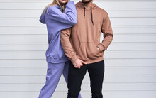 Blonde Girl Is Standing In Blue Sport Outfit. Man Wears Brown Hoodie And Black Pants. Couple Is Wearing Street Matching Outfit