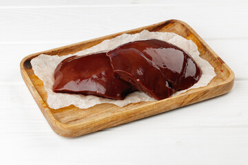 Raw beef liver on wooden board on table