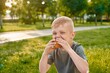 © Hanna - A small five-year-old red-haired boy eats a juicy orange peach in the park, close-up