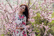 © dmitriisimakov - Beautiful brunette woman in a dress with flowers walks through the flowering garden in spring
