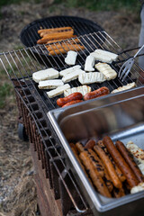 Barbequing sausages on hot coals outside, two grills with meat, cheese and sausages