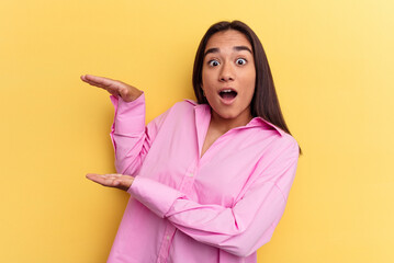 Wall Mural - Young mixed race woman isolated on yellow background shocked and amazed holding a copy space between hands.