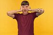 © timtimphoto - Indoor shot of irritated tired young male student, closed his ears with arms, shouting and want silence. Isolated over yellow background