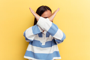 Wall Mural - Young mixed race woman isolated on yellow background keeping two arms crossed, denial concept.