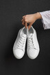 White sneakers in female hand at black background