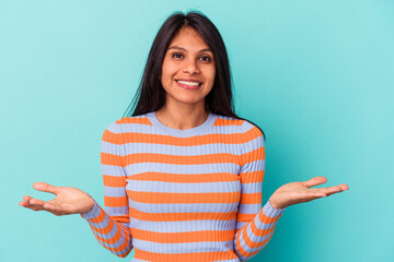 Young latin woman isolated on blue background makes scale with arms, feels happy and confident.