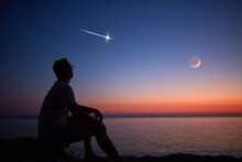 Silhouette Of A Man Looking At The Moon And Stars Over Sea Ocean Horizon.