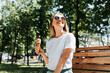 © Sergio - Joyful young woman relaxing on a park bench looking up enjoying the sun and summer weather. Cute smiling girl eating ice cream in a waffle cone, outdoors. Summer lifestyle
