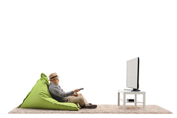 Sticker - Full length shot of a senior gentleman with a remote controller sitting on a bean-bag chair and watching tv