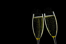 Two Glasses Of Champagne With Splashes Backlit Against A Black Background