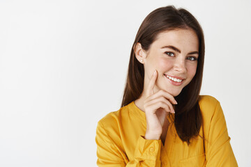 Close-up of attractive brunette in yellow shirt looking at camera, smiling with pleased happy face expression, white background