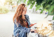 © Soloviova Liudmyla - Portrait of smiling at camera red curled hair caucasian teen girl unlocking bike at Bicycle sharing point using the modern smartphone. Green urban transport and modern technology devices concept image