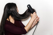 © AliciaFdez - Woman straightening her long black shiny hair using a flat iron with both hands as if it was a weapon. Isolated in a white background