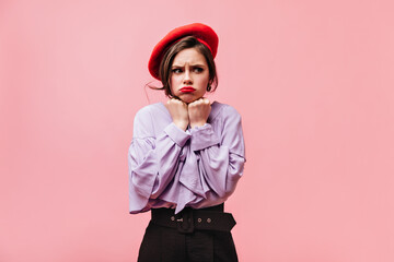 Canvas Print - Nice girl dressed in purple blouse, red beret and pants posing offendedly on pink background