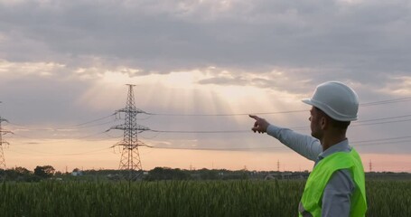 Wall Mural - an engineer looks towards a high-voltage power line and points at it with his index finger.