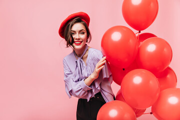 Wall Mural - Beautiful woman in stylish blouse and beret looks into camera with smile. Portrait of girl with red lips posing with balloons