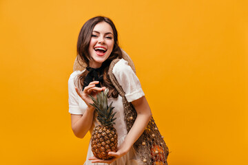 Sticker - Lady in cotton summer dress laughs and poses with pineapple and eco bag on orange background