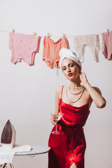 Wall Mural - Gorgeous girl in red silk outfit posing with martini glass on background of clothes