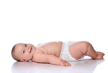 Happy smiling infant child baby girl kid in diaper is lying on her back sideways to camera, touching floor with hand and looking at camera isolated on a white background