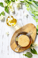 Wall Mural - Therapeutic herbal tea. Hot Jasmine tea with jasmine flowers in a glass teapot on a rustic wooden table. Top view flat lay background.