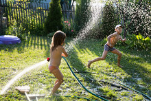 Happy Kids Brother And Sister Playing With Garden Hose And Having Fun With Spray Of Water In Sunny Backyard. Summer Time.