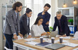 © Studio Romantic - Focused serious people looking at laptop screen standing around office table during group meeting in boardroom. Small business team studying recent trends and changes in modern marketing