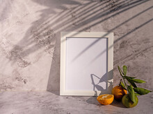 Rectangular White Portrait Frame Mockups With Cut Orange With Green Foliage On White Stone Background. Long Shadows From A Palm Branch, Neutral Color Palette. Artistic Display Concept.
