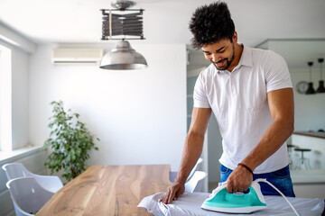 Wall Mural - Happy young handsome black man ironing clothes at home