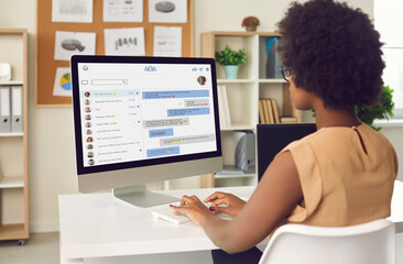 black business lady or team manager sitting at office table, looking at web page on desktop computer