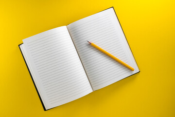 Fototapete - Open lined notebook with yellow pencil isolated on yellow background in top view, flat lay, copy space