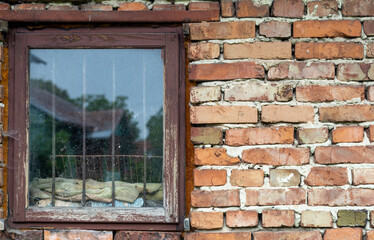 Old brick wall with a wooden window. With metal grilles. Display of an old house in the window