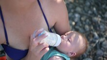 Young Mother With Newborn Cute Infant Baby Boy, Holding Him On Arms, Hugging And Feeding With Bottle Breast Milk Outside In Sunny Day. Healthy Child, Concept Of Hospital And Happy Motherhood. Nursery.