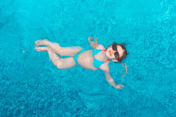 little girl in sunglasses swims in a swimming pool with blue water on a summer day