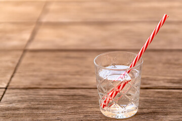 Glass of soda water with red white striped straw on wooden table. Refreshing non-alcoholic drink for hot summer days to stay hydrated for detox diet and healthy nutrition. Background with copy space.