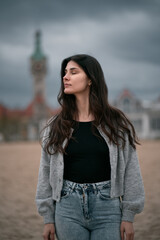 Poster - Sensual and gorgeous brunette on the beach. Clothed woman on the beach during autumn season on the seaside. Portrait of girl with brown hair wearing black shirt and jeans.