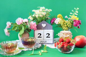 Wall Mural -  Calendar for July 22 : the name of the month of July in English, cubes with the number 22, bouquets of wild flowers, jam, fruit, cups of tea, white napkins, green background