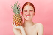 © Look! - Front view of glad woman with pineapple posing with closed eyes. Studio shot of excited ginger girl holding fruit on pink background.