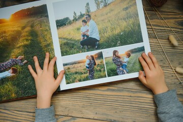 the Hand child holding a family photo album against the background of the a wooden table