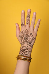 Wall Mural - Woman with beautiful henna tattoo on hand against yellow background, closeup. Traditional mehndi